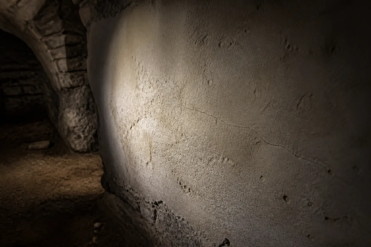 Fissure fine courant sur le mur enduit d&rsquo;une cave voûtée éclairée à la lampe torche